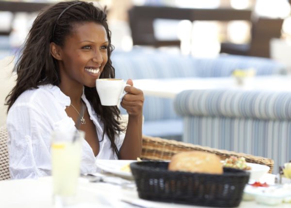 Happy woman eating breakfast, holding cup of coffee in left hand.