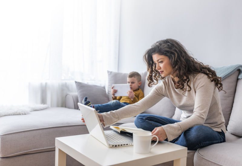 Mother working on laptop at home, while her child using tablet.